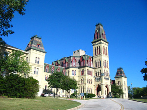 Color photo of a tan building with towers and narrow red windows.