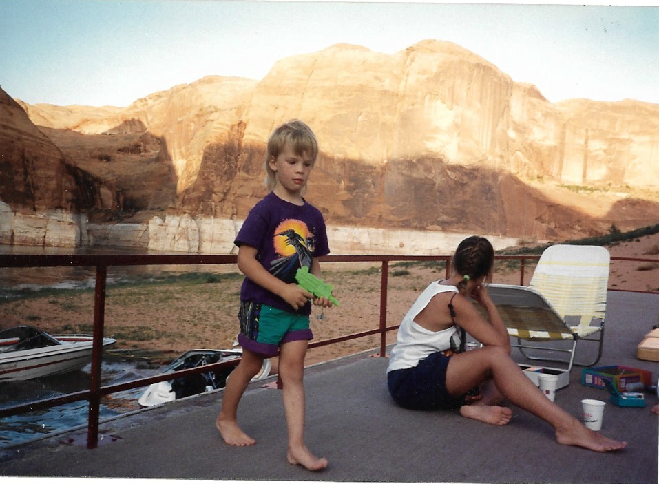 A person sits near a child with a squirt gun on the upper deck of a boat as it is beached near a canyon.