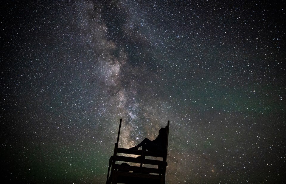 Person sitting in a lifeguard chair gazing into night sky Person sitting in a lifeguard chair gazing into night sky
