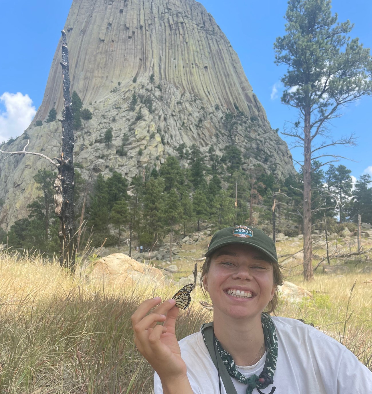 Nina_DETO_creditNinaCrawford A person sitting down gently holding a monarch butterfly with a towering rock formation in the background.