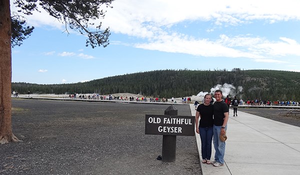“Old Faithful” at Yellowstone National Park Couple stands by sign for Old Faithful Geyser