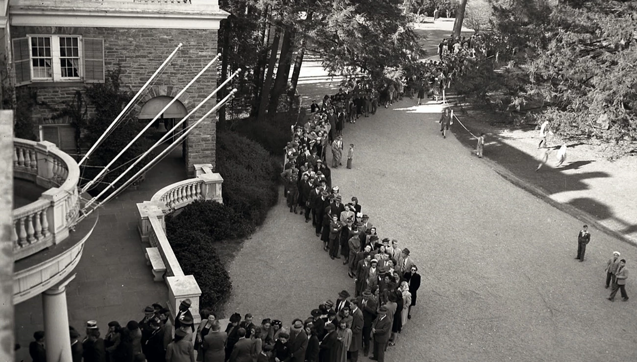 A long line of people waiting to enter a house.