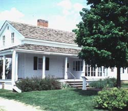 Small, white house with a front porch and tree.