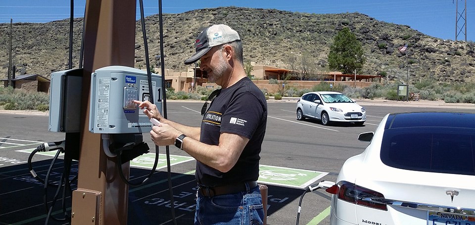 Visitor stands in parking lot and plugs in car to charging station