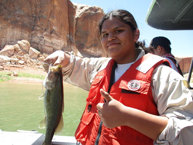A teen on a boat wearing a lifejacket holds up a large fish.
