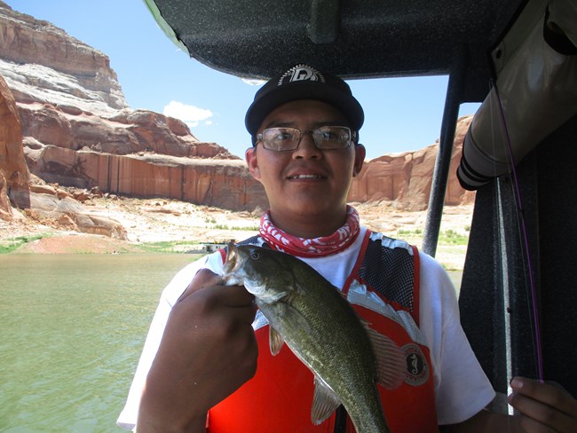 Hershal Yazzie A teen wearing a lifejacket on a boat holds up a large fish.