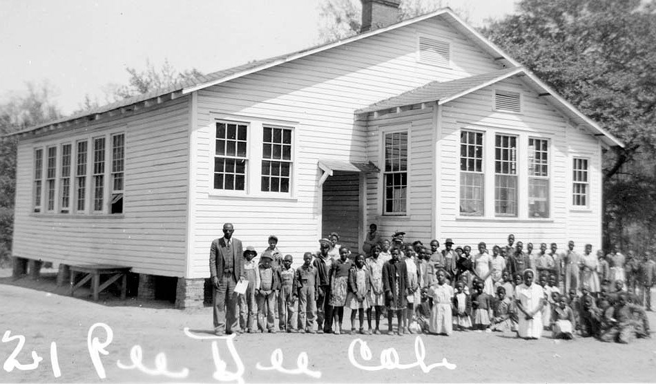 Photo of students in front of an small schoolhouse.