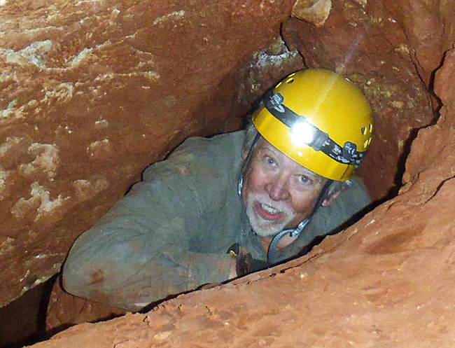 person with helmet in small cave passage