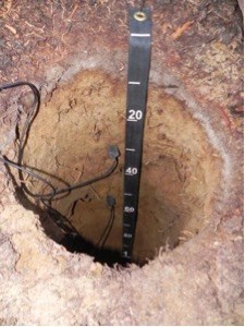 A circular pit in the ground with a few wires and a measuring stick going down into it