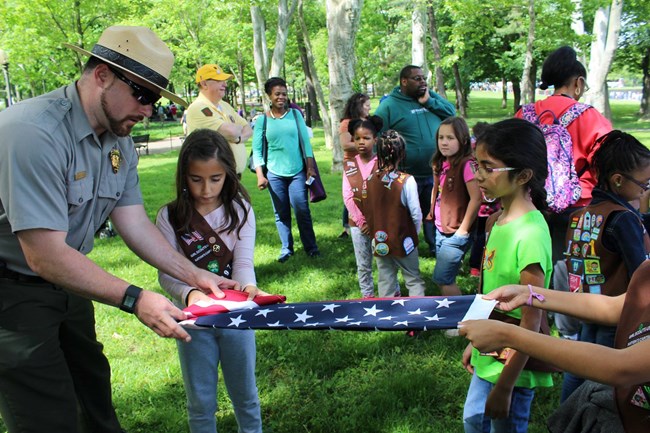 Folding a flag with Girl Scouts A ranger folds an American flag with a group of Girl Scouts
