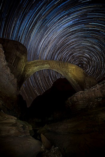 Rainbow Bridge, Dark Sky Sanctuary Night timelapse photo of curved sandstone bridge with starry sky.