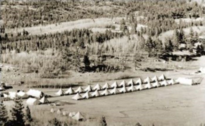 Two rows of tents at the bottom of a hill covered in evergreen trees Two rows of tents at the bottom of a hill covered in evergreen trees