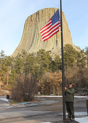 A man raising the American flag with a large rock monolith in the background.