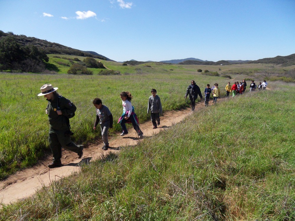 NPS Park Ranger leading a hike with kids on a dirt path in Santa Monica mountains.