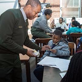 African American male ranger teaches a student at a table.