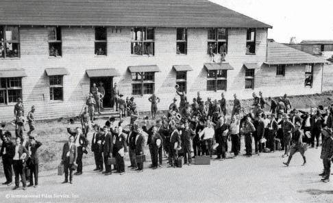 Men in uniform and civilian clothes stand outside a military buliding