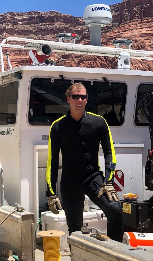 Park Ranger stands near park ranger in a wetsuit on a park boat.
