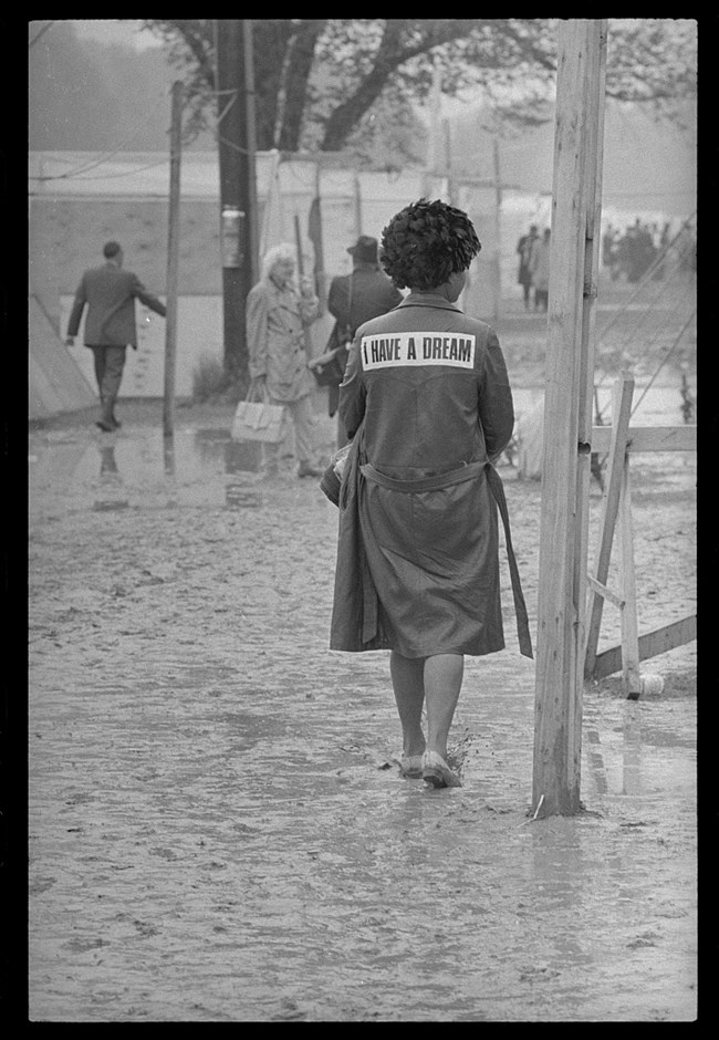 Woman with "I Have A Dream" on the back of her raincoat walks through the mud of Resurrection City