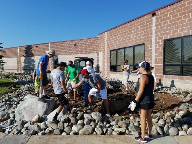 Men and women in proper work attire move rocks and dirt out of the way for the garden