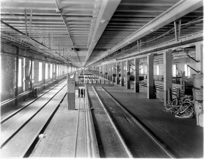 Long, empty room with tracks on the floor, pillars and rope piled in corner