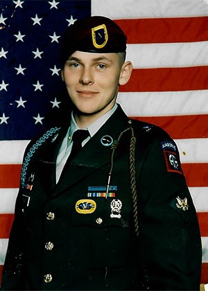 A man in class A military uniform posing in front of the American flag