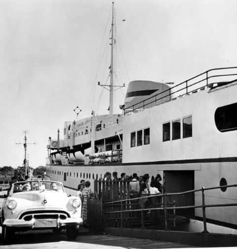 B&W photo pf a white car next to a large white and grey boat.