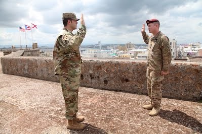 Two men in army fatigues face each other with their right hand raised atop the stone forts in San Juan, Puerto Rico.