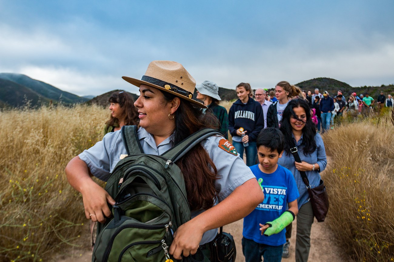 SAMO Tarantula Hike NPS Conanr L'Ecuyer Ranger leading a large group through a dry grassland trail