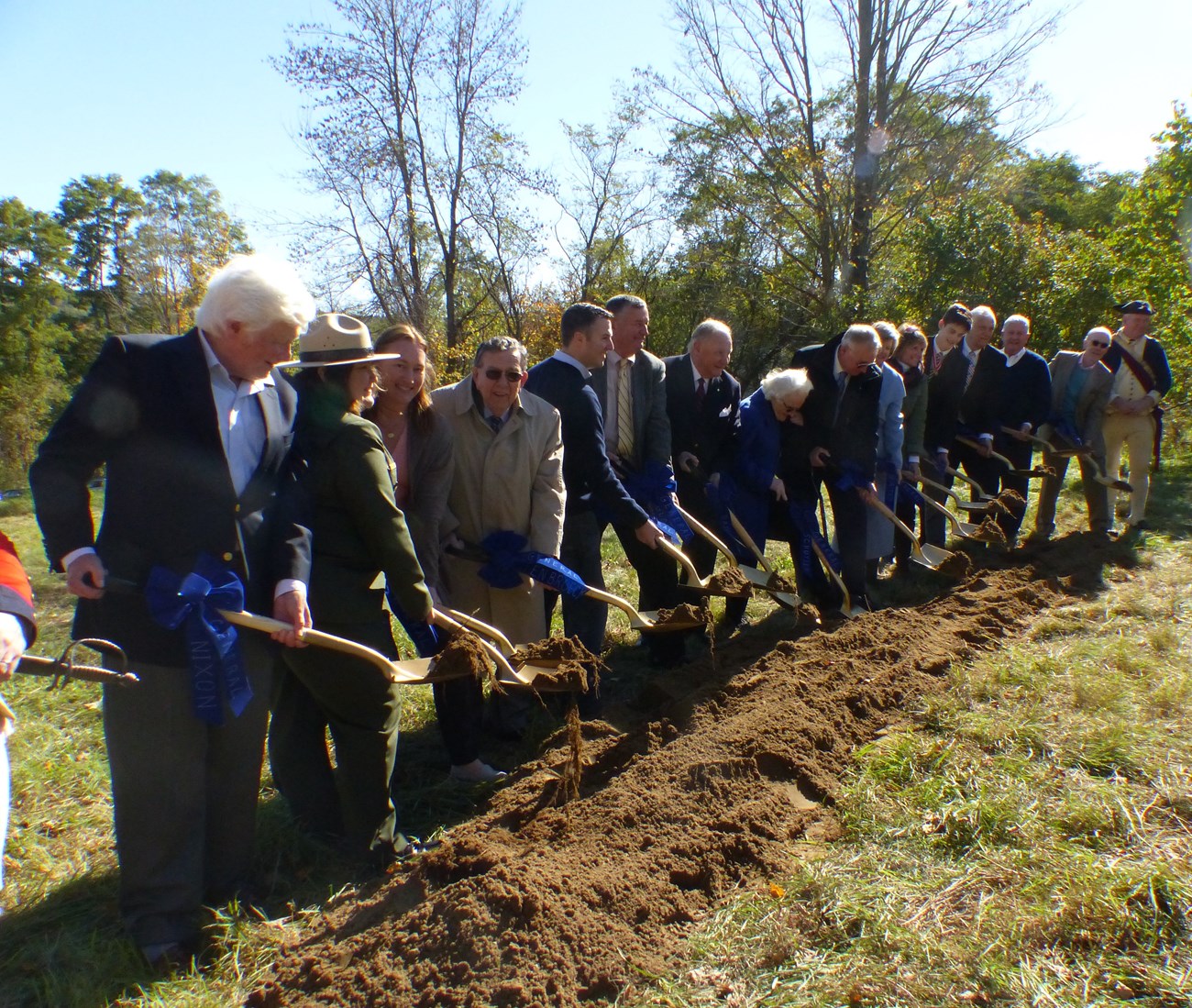 Fifteen people plant shovels in the dirt to break ground for a new monument. Fifteen people plant shovels in the dirt to break ground for a new monument.
