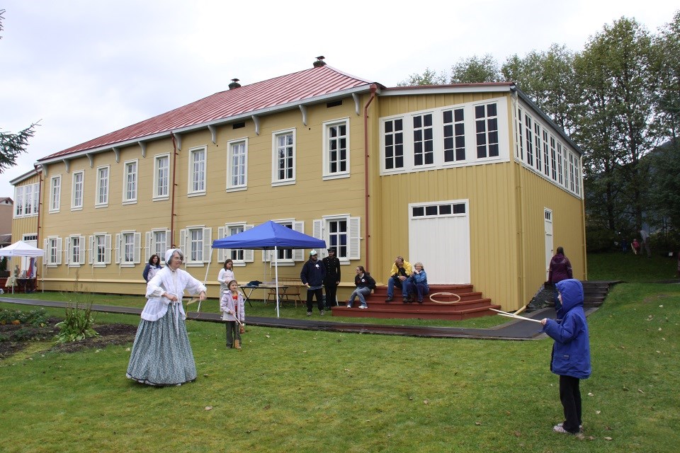 Living historians demonstrating a game to a child in front of a historic yellow house