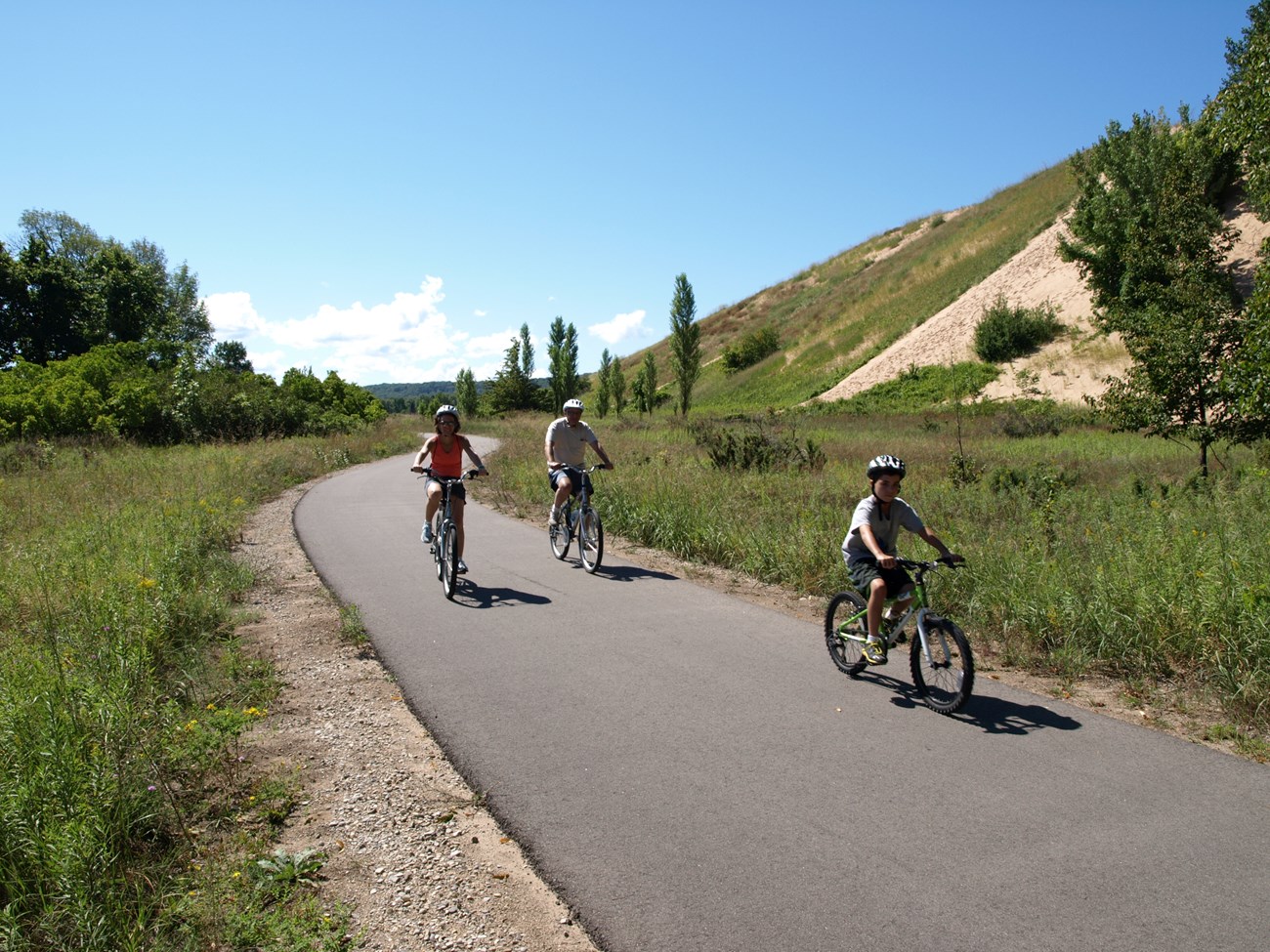 three people ride bikes on a paved trail