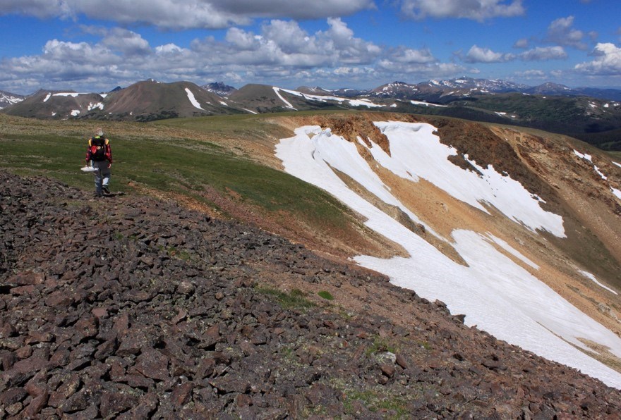 Surveyor walks on rocks and tundra with mountains in the background