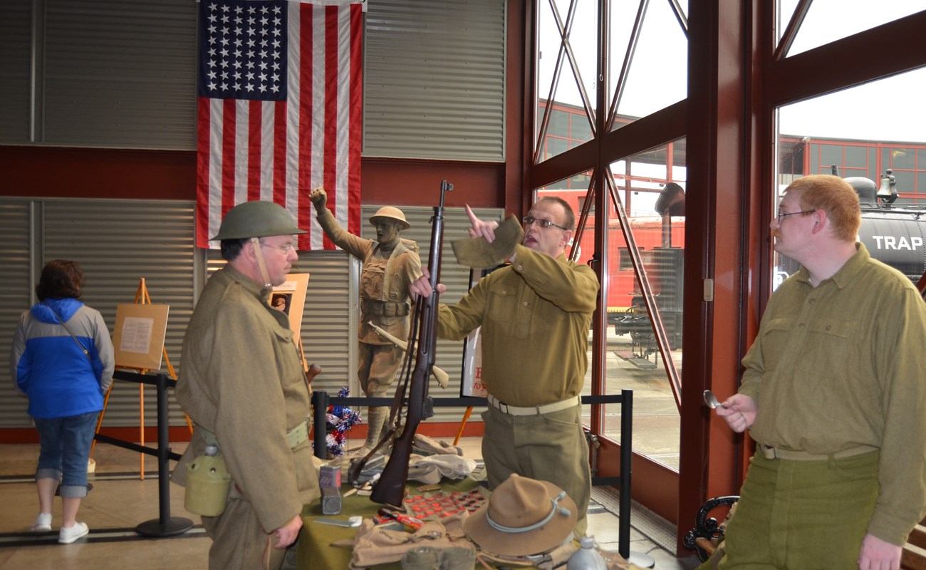 Men in military period costumes with a statue in the background.