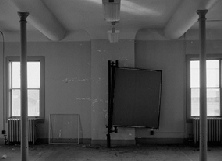 B&W image of two columns, two windows, and two rounded plaster ceiling features on the interior of a building.