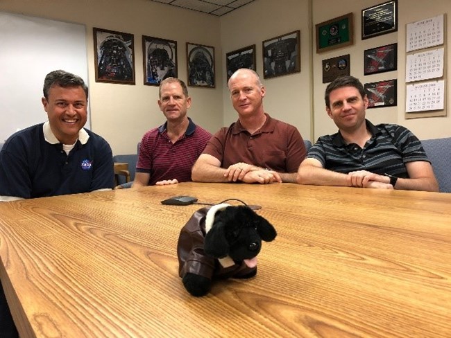 Seaman with pilots toy dog with four men sitting at a table