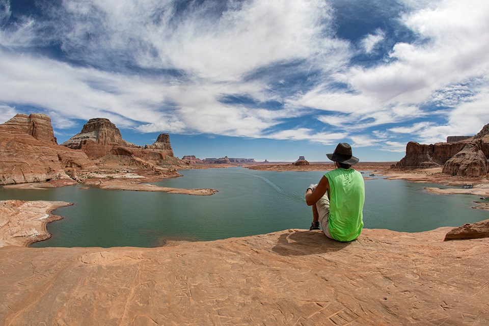 Brent Davis Man sits looking away from camera at lake and sandstone cliffs