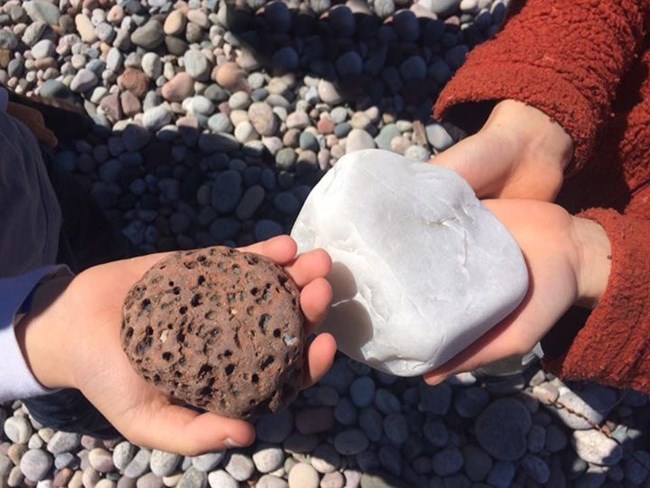 Shows two young hands one holding a rough rock one holding a smooth rock