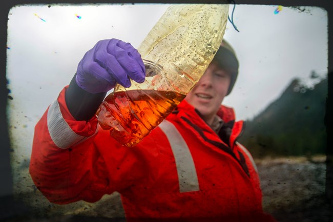 a Park Ranger holds up a plastic water bottle found on the beach.