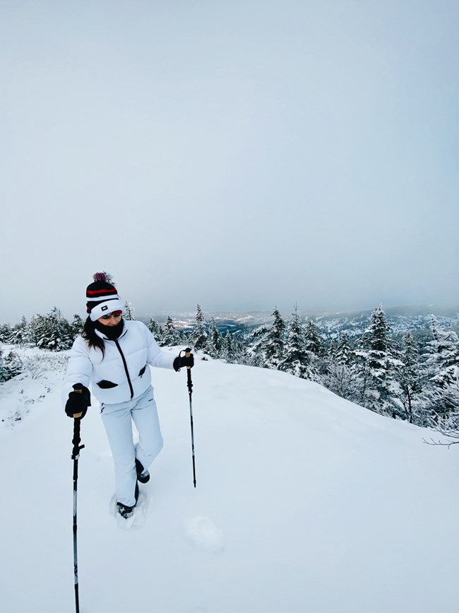 Hiking up Cadillac Mountain in the snow Woman climbing mountain with walking poles