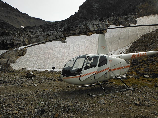 a helicopter parked next to a snow field on a mountainside