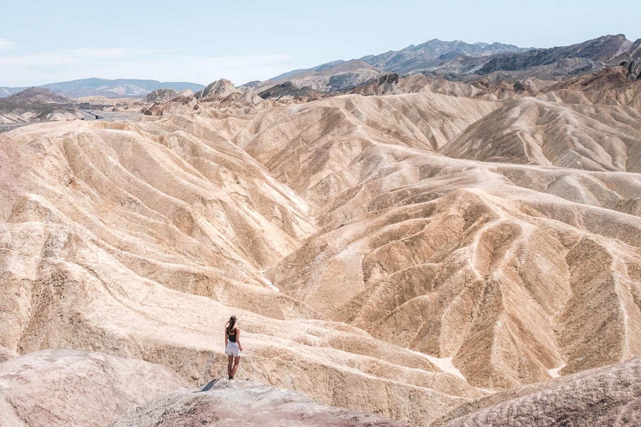 lone woman looks down on badlands with mountains in background