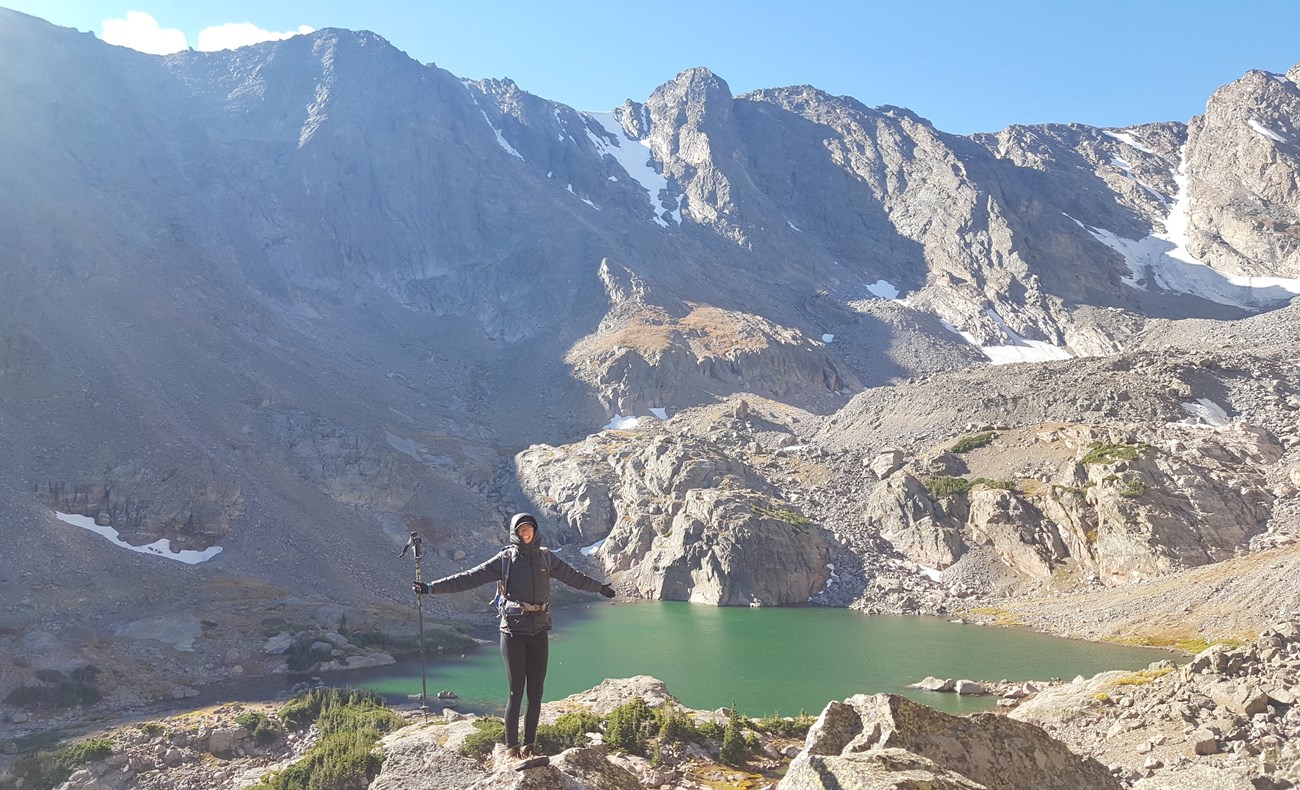 hiker in Rocky Mountain National Park hiker with alpine lake and mountains behind her