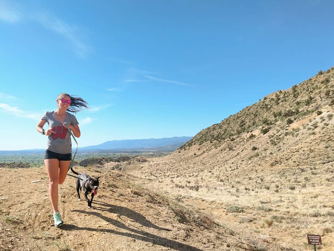 woman and dog run in foothills