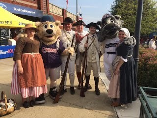 People in period costumes and a costumed bear mascot pose for a photograph.