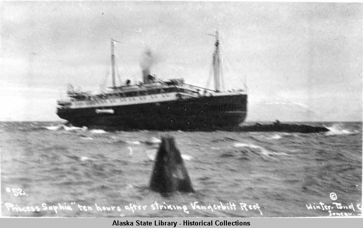 Historical, black and white image of a ship stranded on a reef in choppy ocean water.