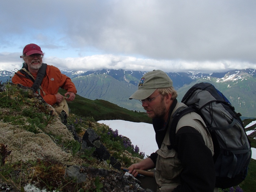 two people look at lichen on a rock on an alpine ridge