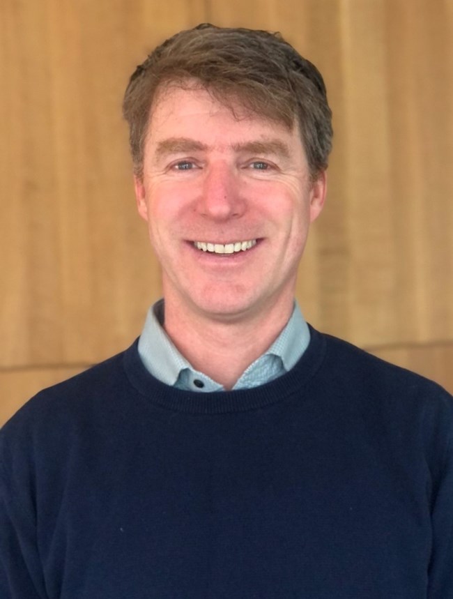 Photo portrait of a man with a blue sweater and brown hair.