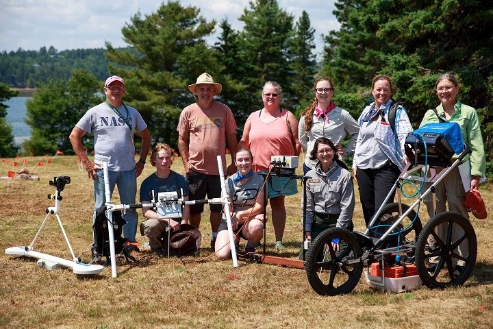 Men and women volunteers and park staff pose with archaeological equipment, outdoors.