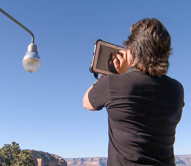 a person holding an iPad is talking a photo of an street lamp.