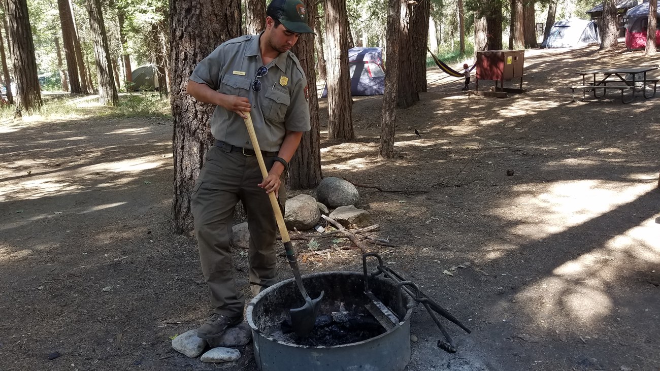 park ranger stirs coals in a campfire ring